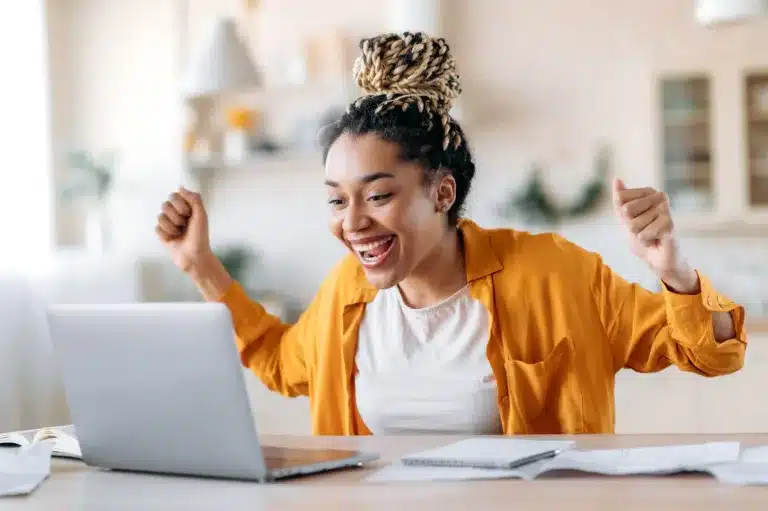 A woman excitedly smiling at a laptop screen