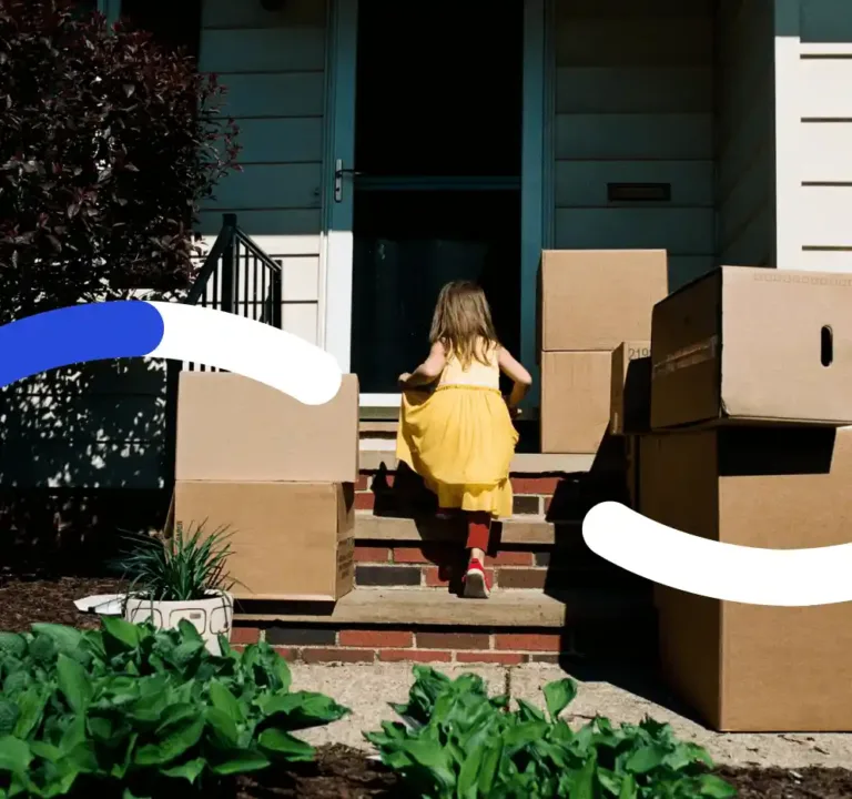 A little girl running up the front steps of a home surrounded by moving boxes